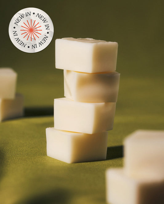 A stack of creamy white wax melts on a green surface, featuring a circular "New In" badge in the top left corner.